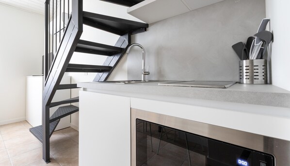 Eine moderne Küche mit eingebautem Geschirrspüler, einer Edelstahl-Spüle und einer schwarzen Treppe.