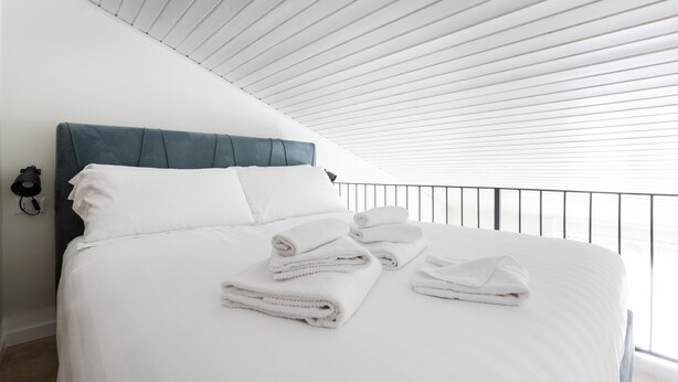 A neatly made bed with white linens and folded towels, a blue upholstered headboard, and a white ceiling with horizontal lines. - Italianway - Metastasio 3 int 58 (Milan)