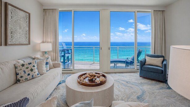 A hotel room with a large balcony, a sofa, a coffee table, and a chair. - Family Favorite Oceanfront Condo Newly Redecorated (Panama City Beach)