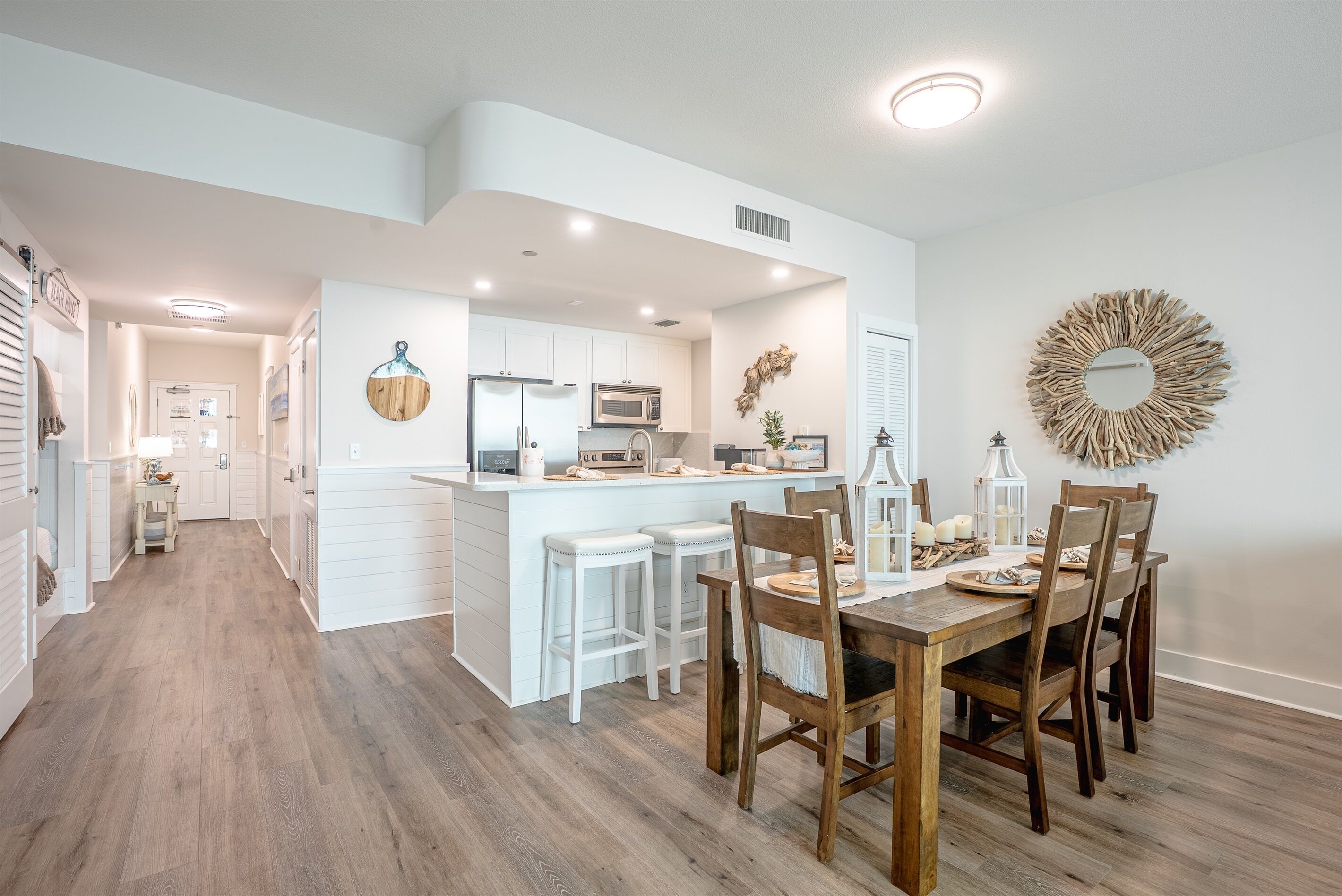 A modern kitchen with white cabinetry, a central island with stools, and a dining area with wooden chairs.