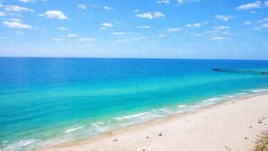 A beach with clear turquoise water, a pier extending into the sea, and a sandy shore with people and umbrellas. - Family Favorite Oceanfront Condo Newly Redecorated (Panama City Beach)