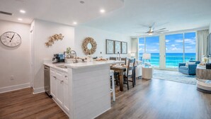 A modern kitchen with a central island, a dining area with a view, and a living room with a large window overlooking the ocean. - Family Favorite Oceanfront Condo Newly Redecorated (Panama City Beach)
