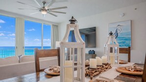 A dining area with a view of the ocean, featuring a ceiling fan, wooden lanterns, candles, and a table set with plates and napkins. - Family Favorite Oceanfront Condo Newly Redecorated (Panama City Beach)