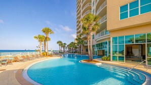 A pool area with lounge chairs and palm trees, surrounded by a building with large windows and balconies. - Family Favorite Oceanfront Condo Newly Redecorated (Panama City Beach)