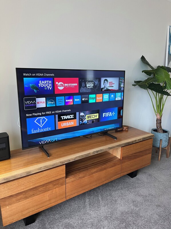 A flat-screen TV on a wooden TV stand displaying various streaming channels. - Mounts Bay Stay Two Bedroom Apt.   Near Kings Park - Free Parking - Wi-Fi (Perth)