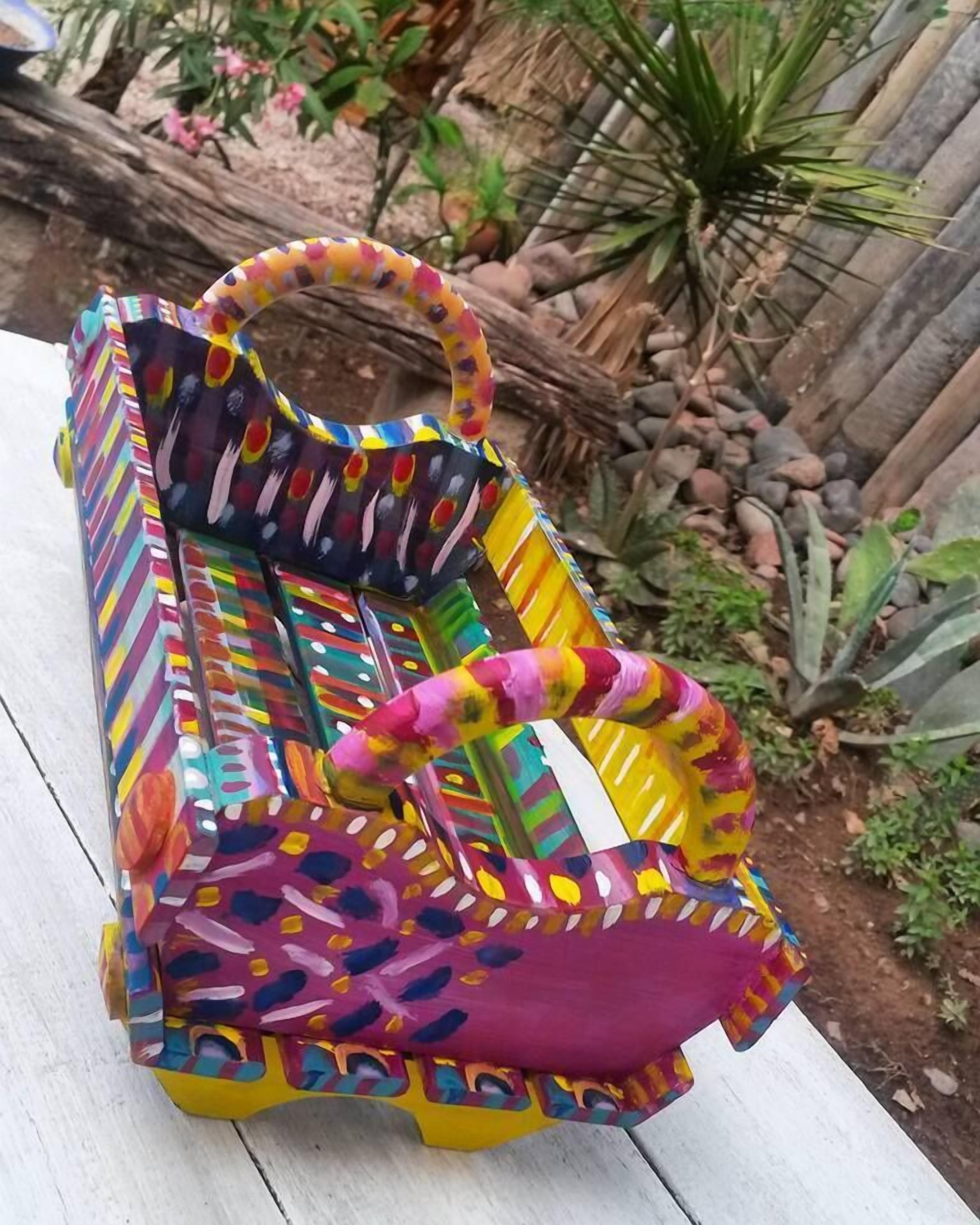 Un banco colorido con diseño, con respaldo y apoyabrazos curvos, situado sobre una terraza de madera.