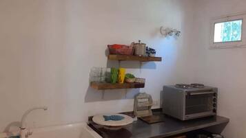 Een kleine kitchenette met een spoelbak, een magnetron en planken met keukengerei.