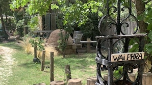 A rustic outdoor setting with a wooden fence, a metal sign reading "Wai Phra," and a garden area with a table and chairs. - Dark Green House - Chacras de Coria (Chacras de Coria)