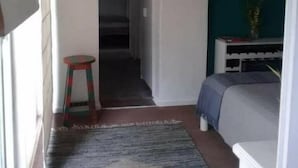 A compact room with a bed, a small stool, a door leading to a hallway, and a wall with framed pictures. - Dark Green House - Chacras de Coria (Chacras de Coria)