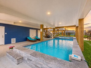 An indoor swimming pool with steps leading into it, lounge chairs, and a view of the surrounding area.