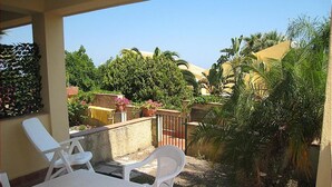 A patio with a table and chairs, surrounded by greenery and a view of a residential area. - Apartment Type A in Costa Saracena - Castelluccio (Augusta)
