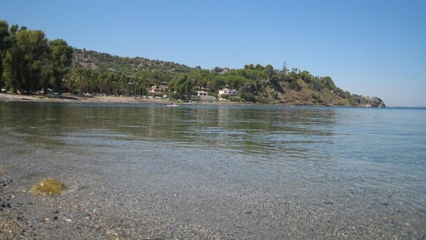 A beach with clear water, pebbles, and a hillside with trees and buildings. - Apartment Type A in Costa Saracena - Castelluccio (Augusta)