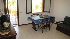 A dining area with a table, chairs, and a television on a wooden table. - Apartment Type A in Costa Saracena - Castelluccio (Augusta)