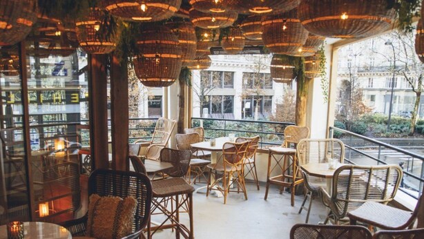 An indoor seating area with wicker furniture and hanging baskets, large windows offering a view of the city. - The Little Rousseau - Cosy & Calm byMon Petit Faré (Paris)