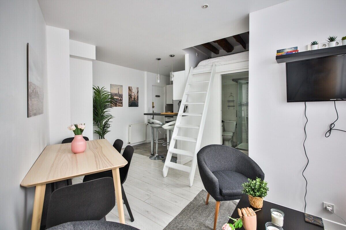 A modern, compact living space with a dining area, kitchen, and a loft bedroom with a ladder.