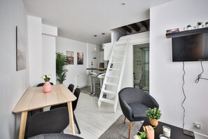 Ett modernt och kompakt bostadsutrymme med matplats, kök och ett sovloft som nås via en stege.