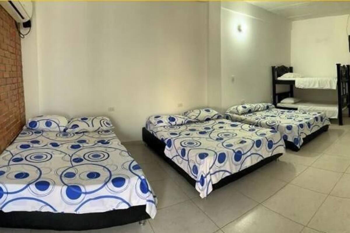 A room with four beds, a kitchen area with a refrigerator, and a television mounted on the wall.