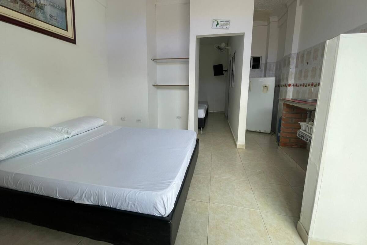 A bedroom with a bed, a hallway leading to a kitchen, and a door with a sign.