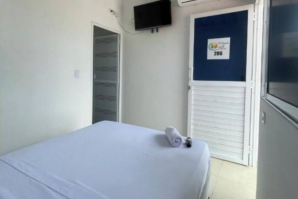 A room with a bed, a TV mounted on the wall, an air conditioning unit, and a door with a number sign.