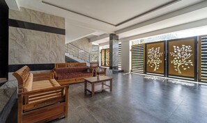 A spacious lobby with a marble wall, a wooden bench, a sofa, and a staircase. - Treebo The Regalia Rooms With Mountain View (Kodaikanal)