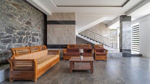 A spacious lobby with a stone wall, a marble column, a staircase, and wooden furniture. - Treebo The Regalia Rooms With Mountain View (Kodaikanal)