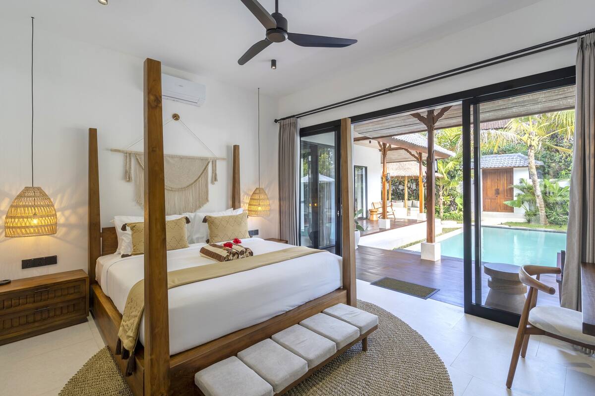 Quarto com cama grande, ventilador de teto e vista para uma piscina.