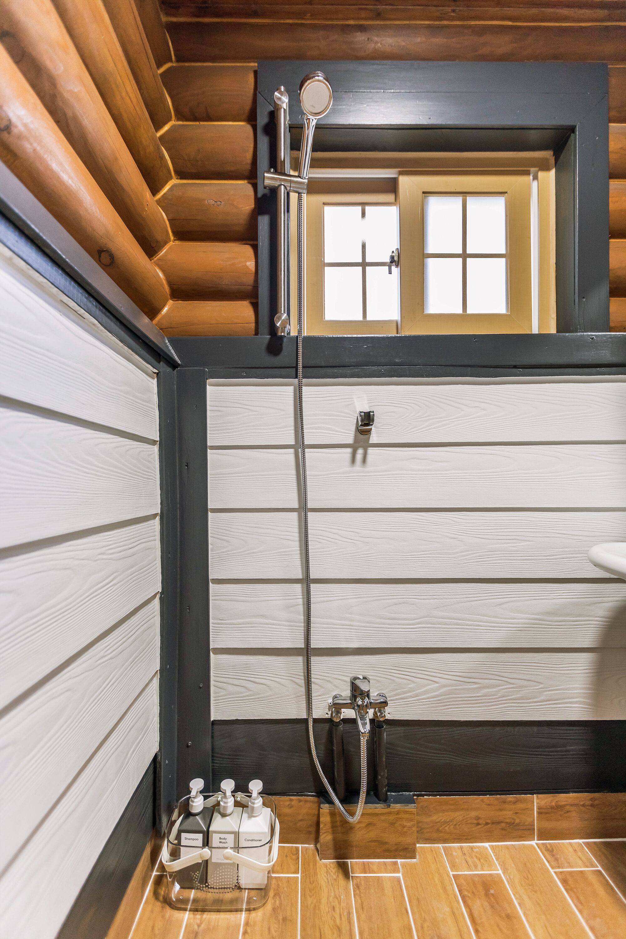 Baño de cabaña de madera con ducha, inodoro y lavabo.
