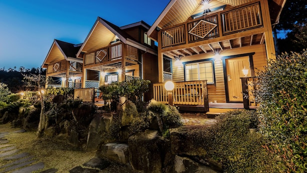 A multi-story wooden house with balconies and a stone pathway leading to the entrance. - Habada Pension (Seogwipo)