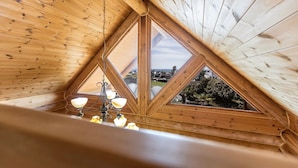A wooden attic room with a sloped ceiling, a chandelier, and large windows offering a view of the outdoors. - Habada Pension (Seogwipo)