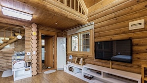 A wooden cabin interior with a kitchen area, a dining table, and a television mounted on the wall. - Habada Pension (Seogwipo)