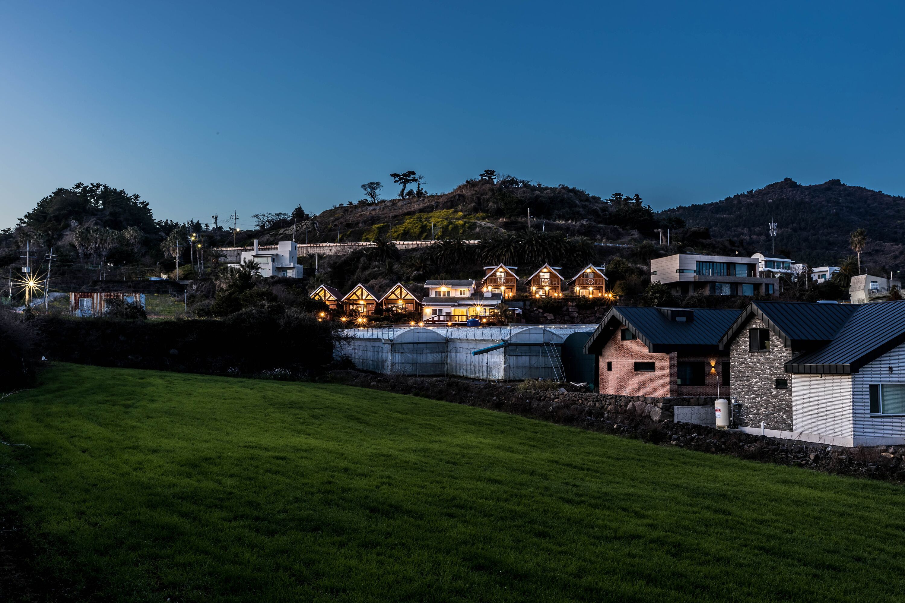 Ett bostadsområde med hus, en gräsyta och en kulle i bakgrunden.
