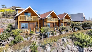 A row of wooden cabins with balconies, set on a rocky hillside with various shrubs and trees. - Habada Pension (Seogwipo)