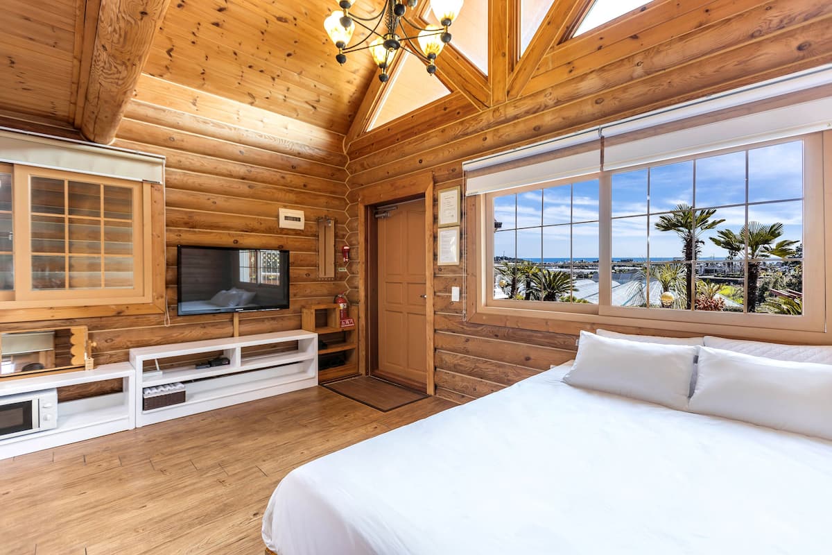 A wooden cabin bedroom with a bed, TV, and large windows overlooking a scenic view.