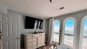 Ein Schlafzimmer mit Bett, Schminktisch, Fernseher und großen, bogenförmigen Fenstern mit Blick.