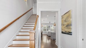 Una escalera de madera con barandilla, que conduce a una zona de cocina con salpicadero y un cuadro en la pared.