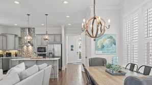 Una cocina moderna con luces colgantes, un comedor con mesa de madera y vistas al exterior a través de una ventana.