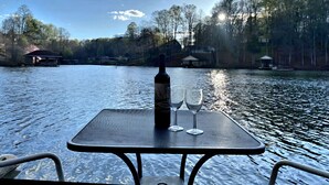 A table with a bottle and two glasses on a boat, overlooking a calm lake with trees and buildings in the background. - Something Special - Firepit / Game/Movie Room / Dock (Moneta)