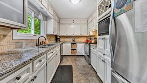 A modern kitchen with white cabinets, granite countertops, stainless steel appliances, and a black mat in the center. - Something Special - Firepit / Game/Movie Room / Dock (Moneta)