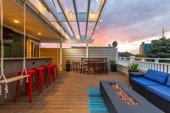 A rooftop patio with a bar area, seating, and a fire feature.