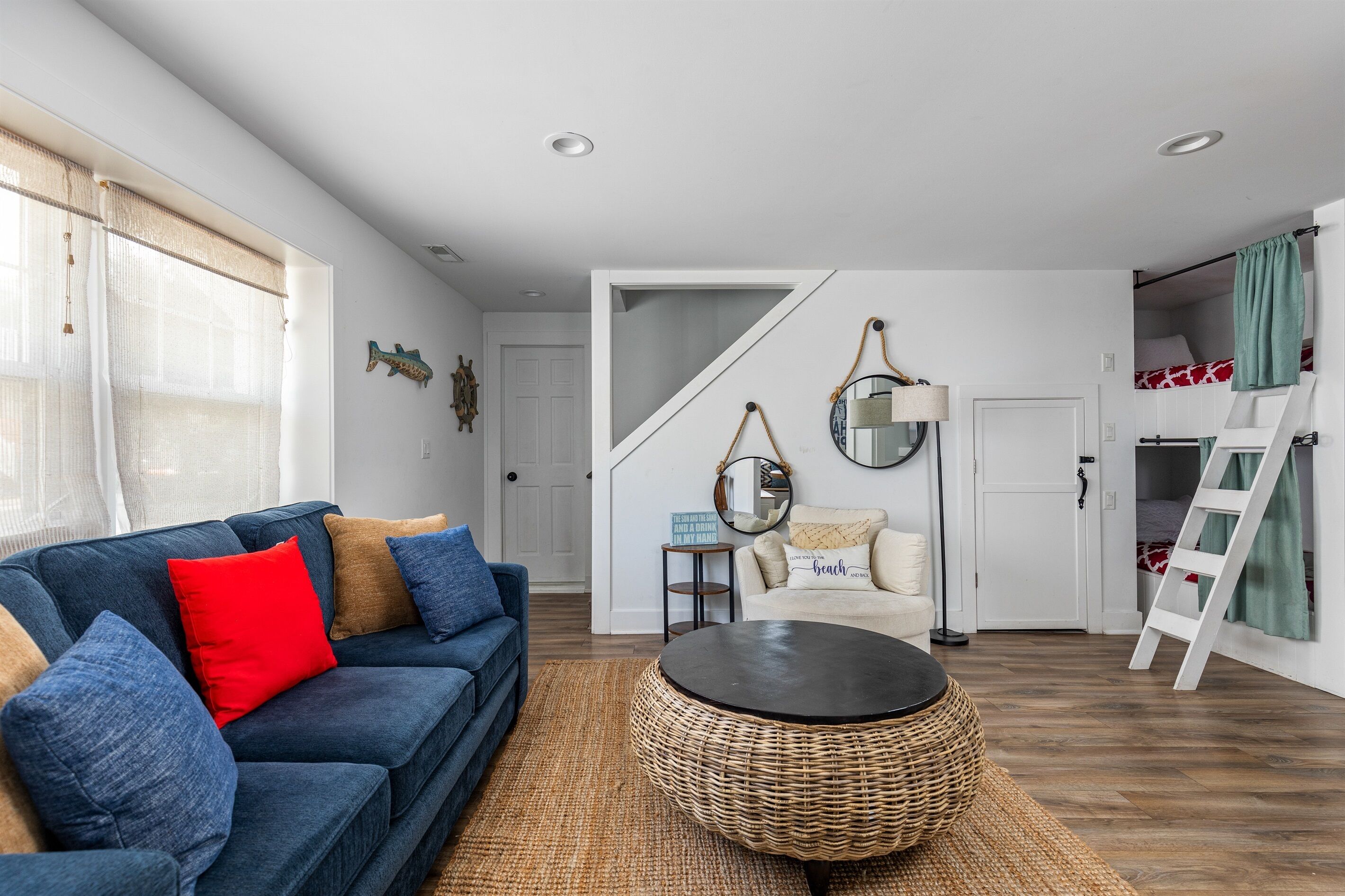 Ein Wohnzimmer mit einem blauen Sofa, einem runden Kaffeetisch aus Weidengeflecht und einer Treppe, die zu einem Schlafzimmer auf dem Dach führt.