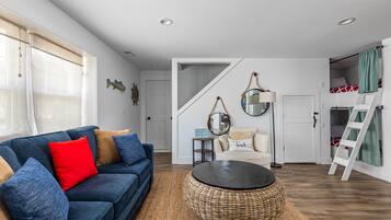 Ein Wohnzimmer mit einem blauen Sofa, einem runden Kaffeetisch aus Weidengeflecht und einer Treppe, die zu einem Schlafzimmer auf dem Dach führt.