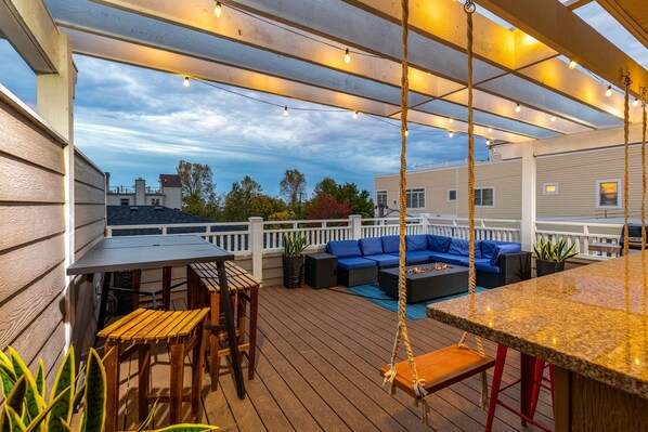 An outdoor deck with a wooden table, chairs, a swing, and a bar area.