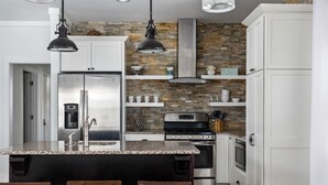 Una cocina con gabinetes blancos, encimera de granito, refrigerador de acero inoxidable, estufa y pileta.