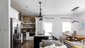 Una cocina moderna con un refrigerador de acero inoxidable, un horno empotrado y un protector contra salpicaduras de piedra. Hay una zona de comedor con una mesa de madera y bancos.