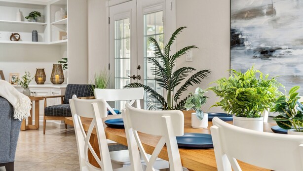 A dining area with a wooden table, white chairs, and potted plants. - Luxury Home, Large Heated Pool, 5-Min to the Beach! (Seminole)