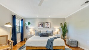 A modern bedroom with a wooden bed, a bedside table with a lamp, a bench, and a potted plant. - Luxury Home, Large Heated Pool, 5-Min to the Beach! (Seminole)