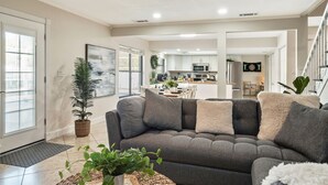 A modern living room with a gray sectional sofa, a ceiling fan, and a view into the kitchen. - Luxury Home, Large Heated Pool, 5-Min to the Beach! (Seminole)