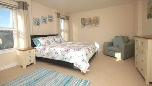 A bedroom with a bed, a grey sofa, a dresser, and a window.