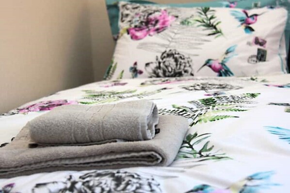 A neatly made bed with floral bedding and a folded towel.