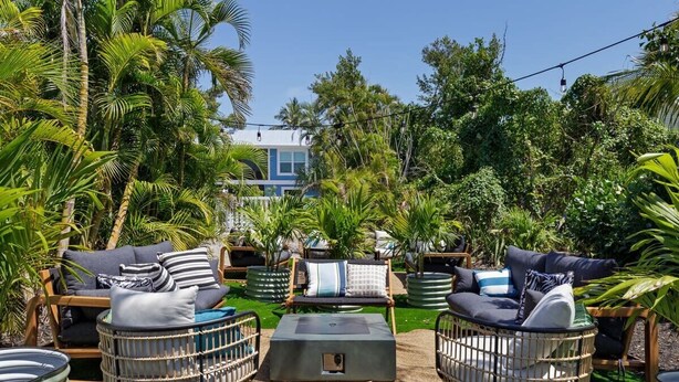 Un espacio al aire libre con mobiliario de mimbre, una mesa central y exuberante vegetación tropical.